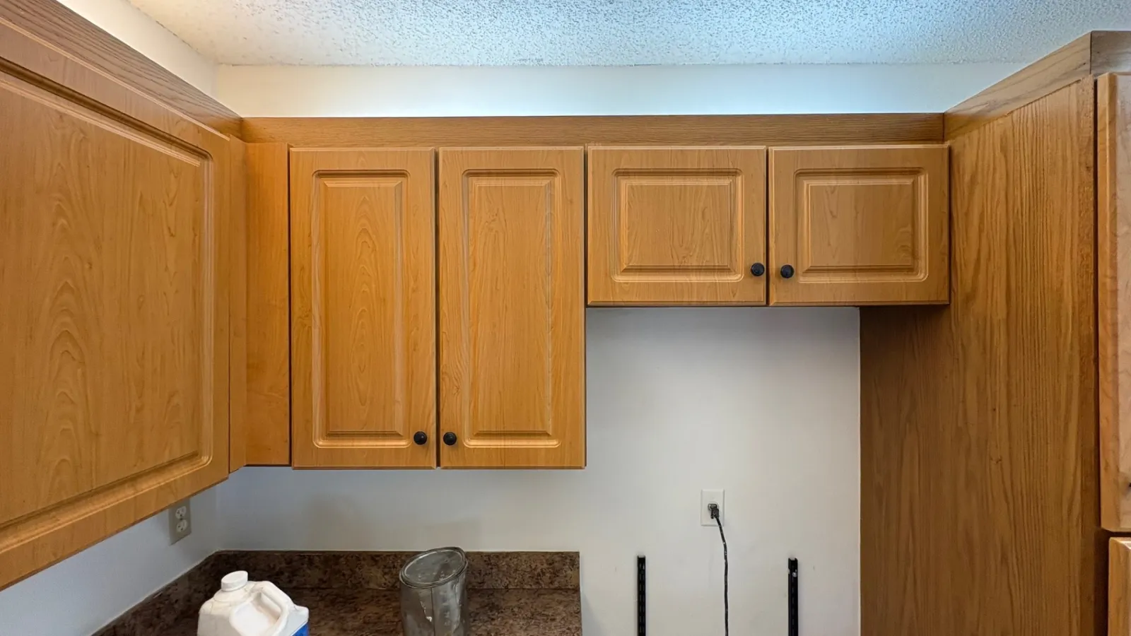 Empty kitchen space with wooden cabinets, granite countertop, and disconnected appliances against white wall.