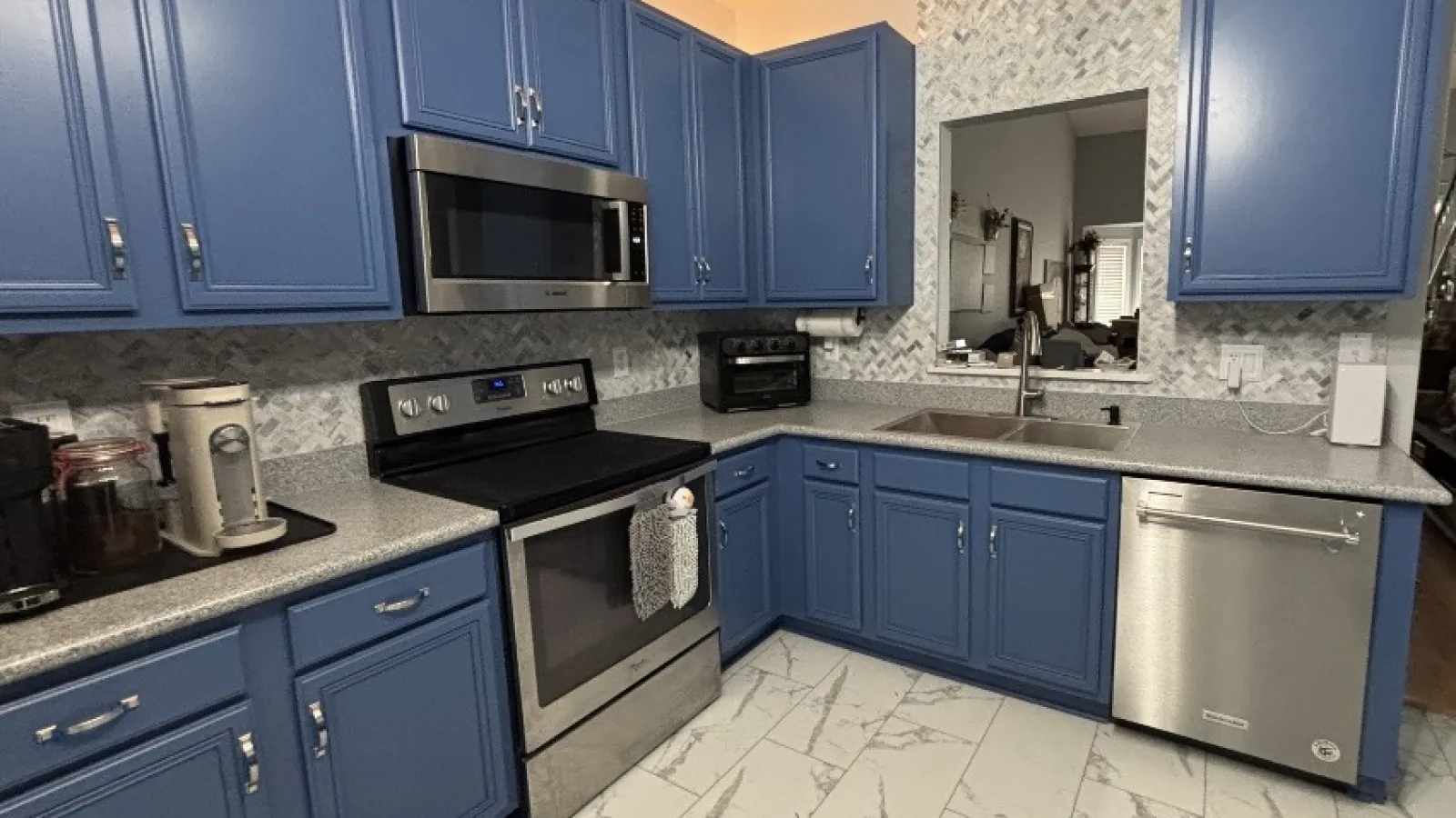 Modern kitchen with blue cabinets, stainless steel appliances, gray countertops, and white marble tile flooring.