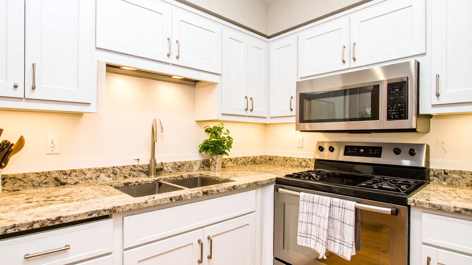 Modern kitchen with white cabinetry, granite countertops, double sink, stainless steel stove and microwave.