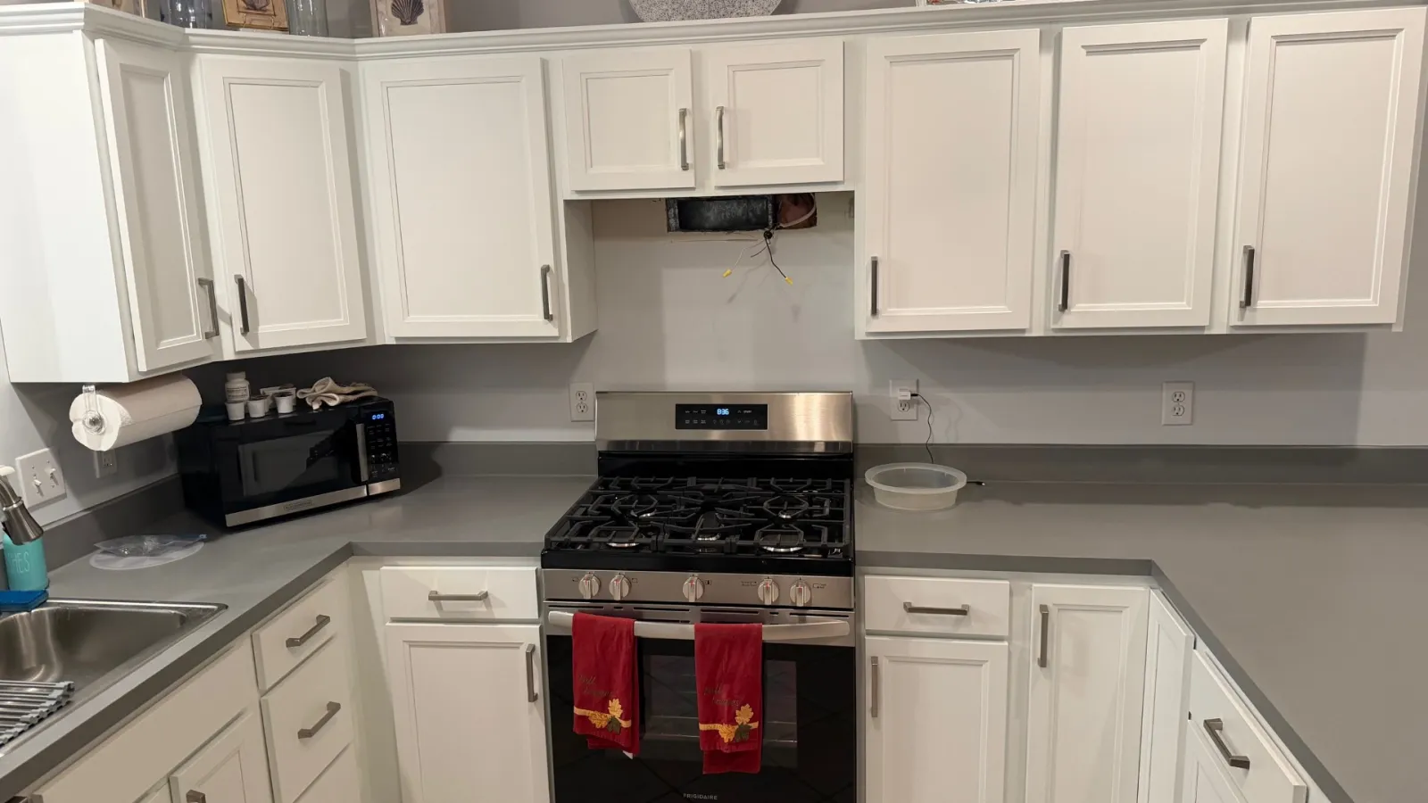 Modern kitchen with white cabinets, gray countertops, stainless steel gas stove, and microwave oven with red towels.