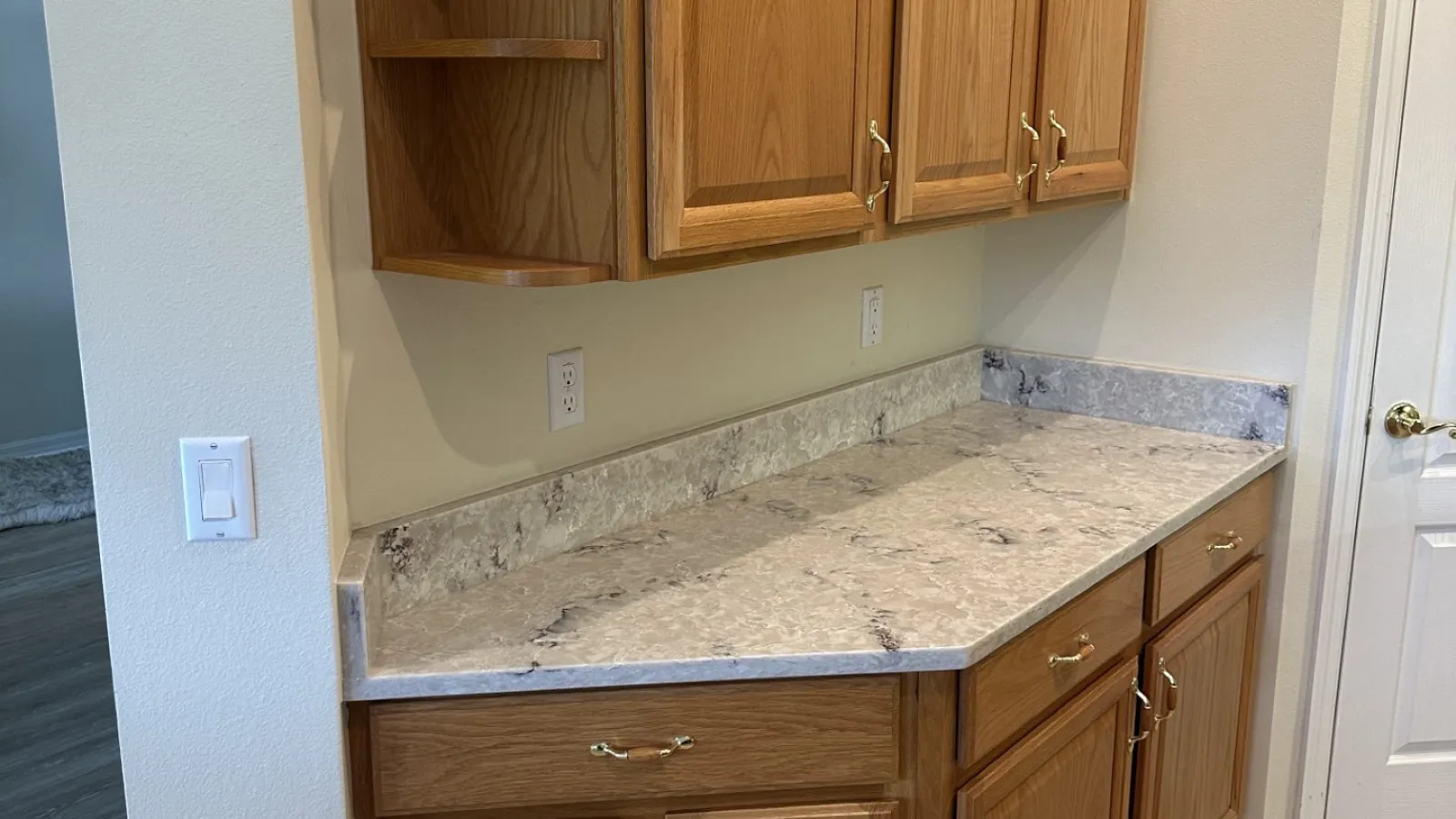 Wooden kitchen cabinets with marble countertop and light hardwood flooring in a neutral tone room.