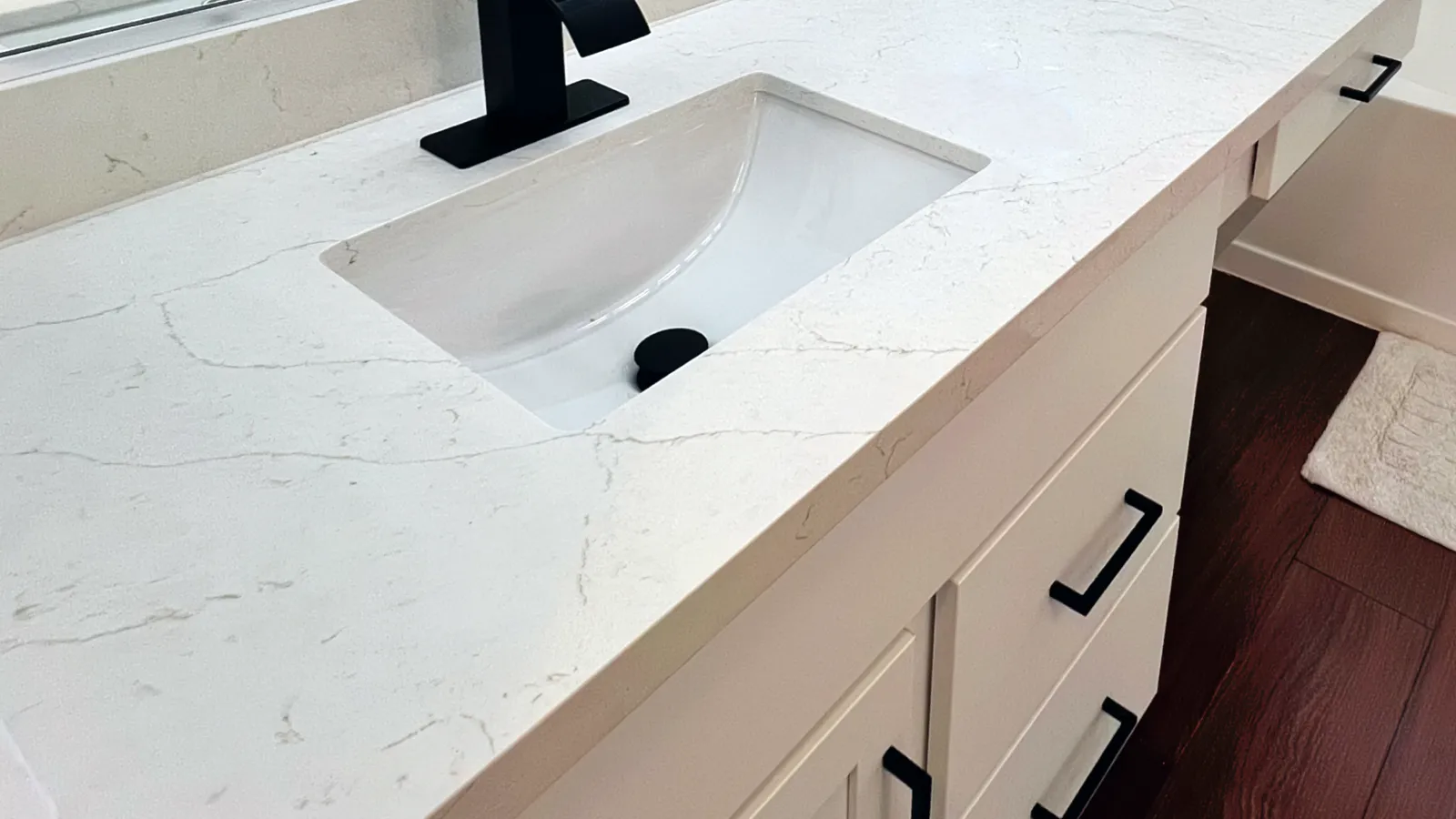 Modern white bathroom vanity with black faucet, white marble countertop, and dark wood flooring.