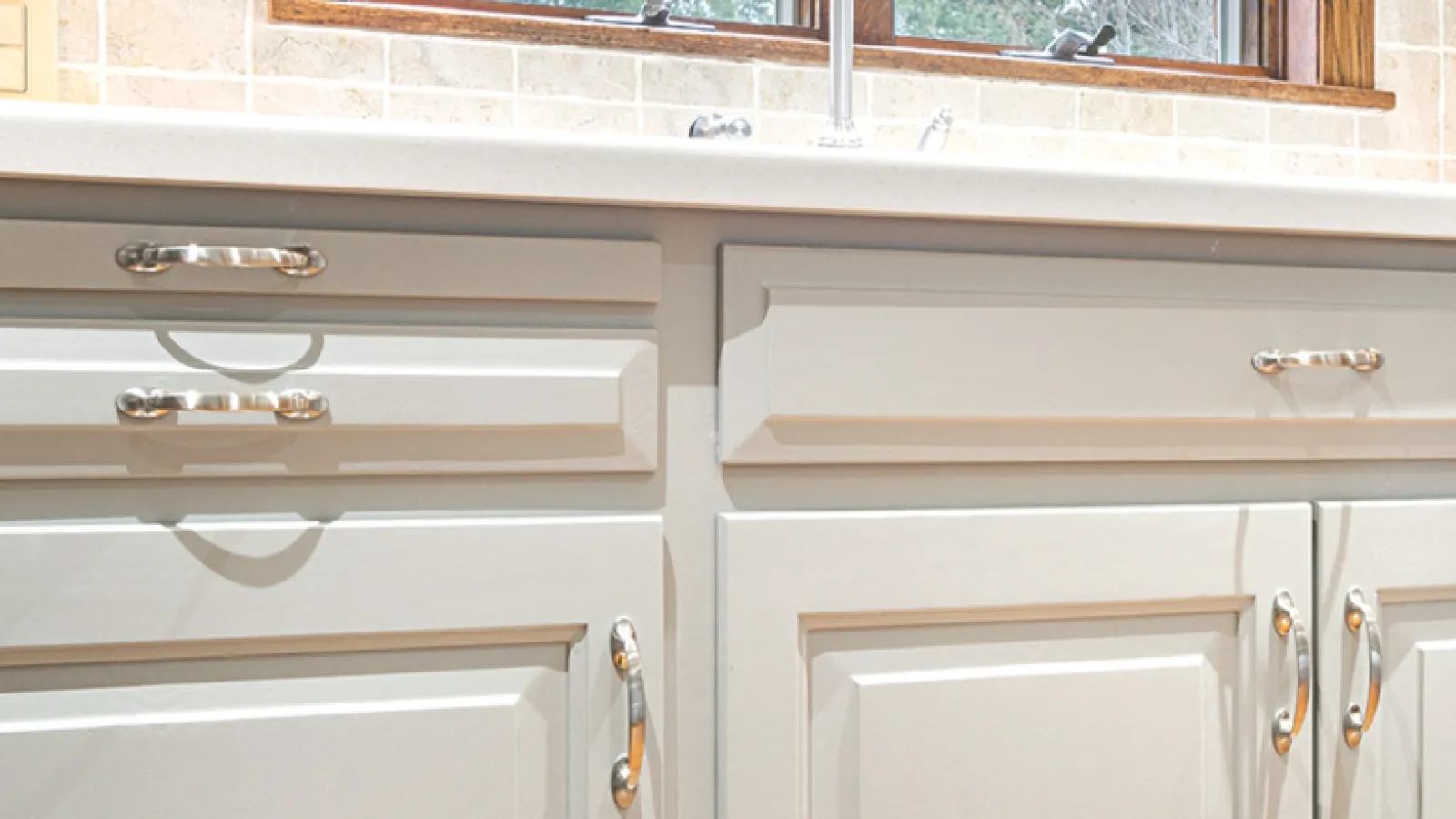 Close-up of white kitchen cabinets with silver handles under a beige tiled backsplash and countertop.