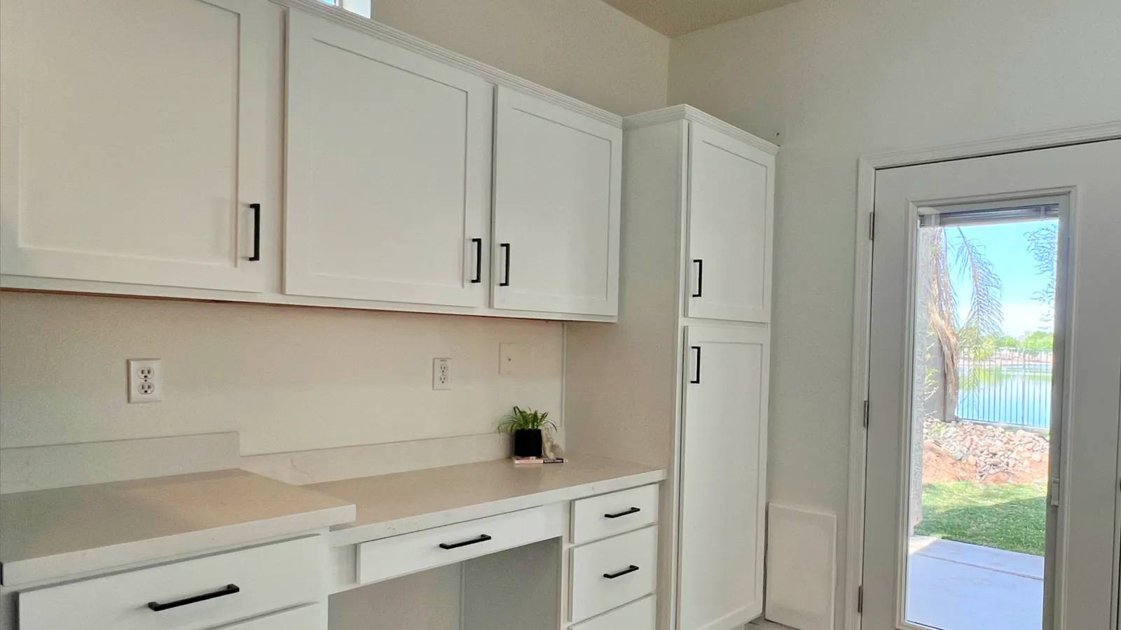 Bright modern kitchen with white cabinets, black handles, dark wood floor, and a glass door leading outside.