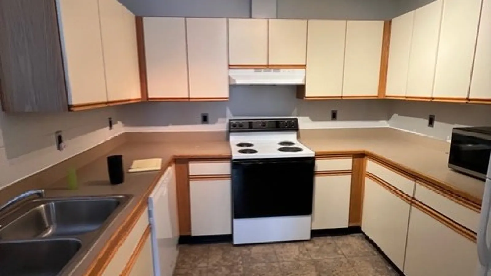 Spacious kitchen with white cabinets, black and white electric stove, double sink, beige countertops, and tiled floor.