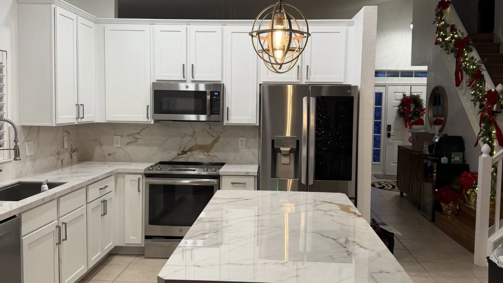 Modern kitchen with white cabinets, marble countertops, stainless steel appliances, and a decorative hanging light fixture