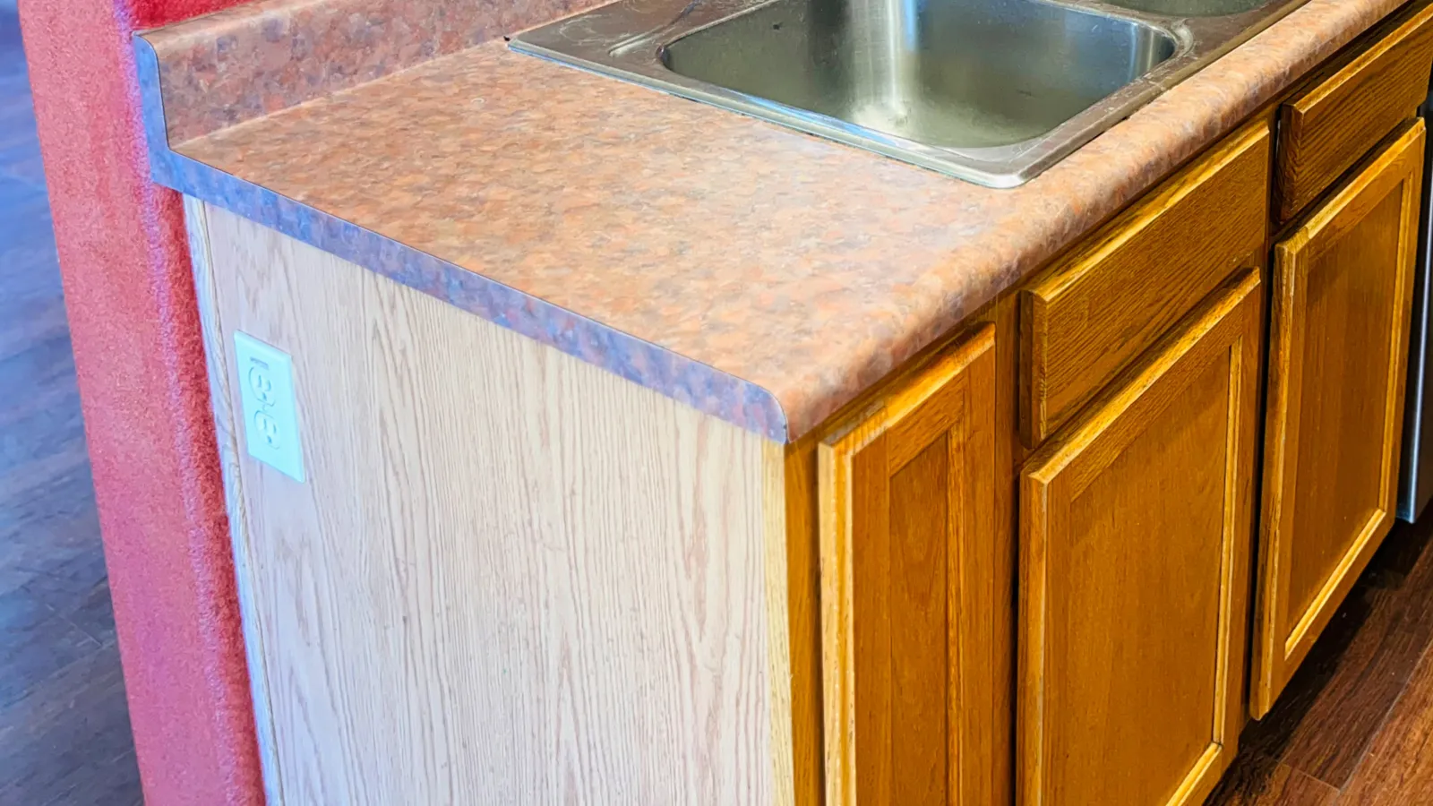 Kitchen counter with brown laminate countertop, double stainless steel sink, wooden cabinets, and red wall.