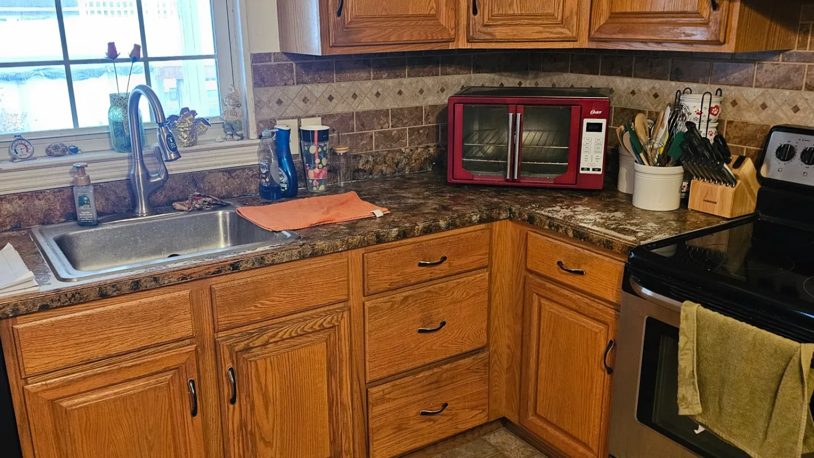 Modern kitchen with wooden cabinets, granite countertops, stainless steel appliances, and tiled floor near window.