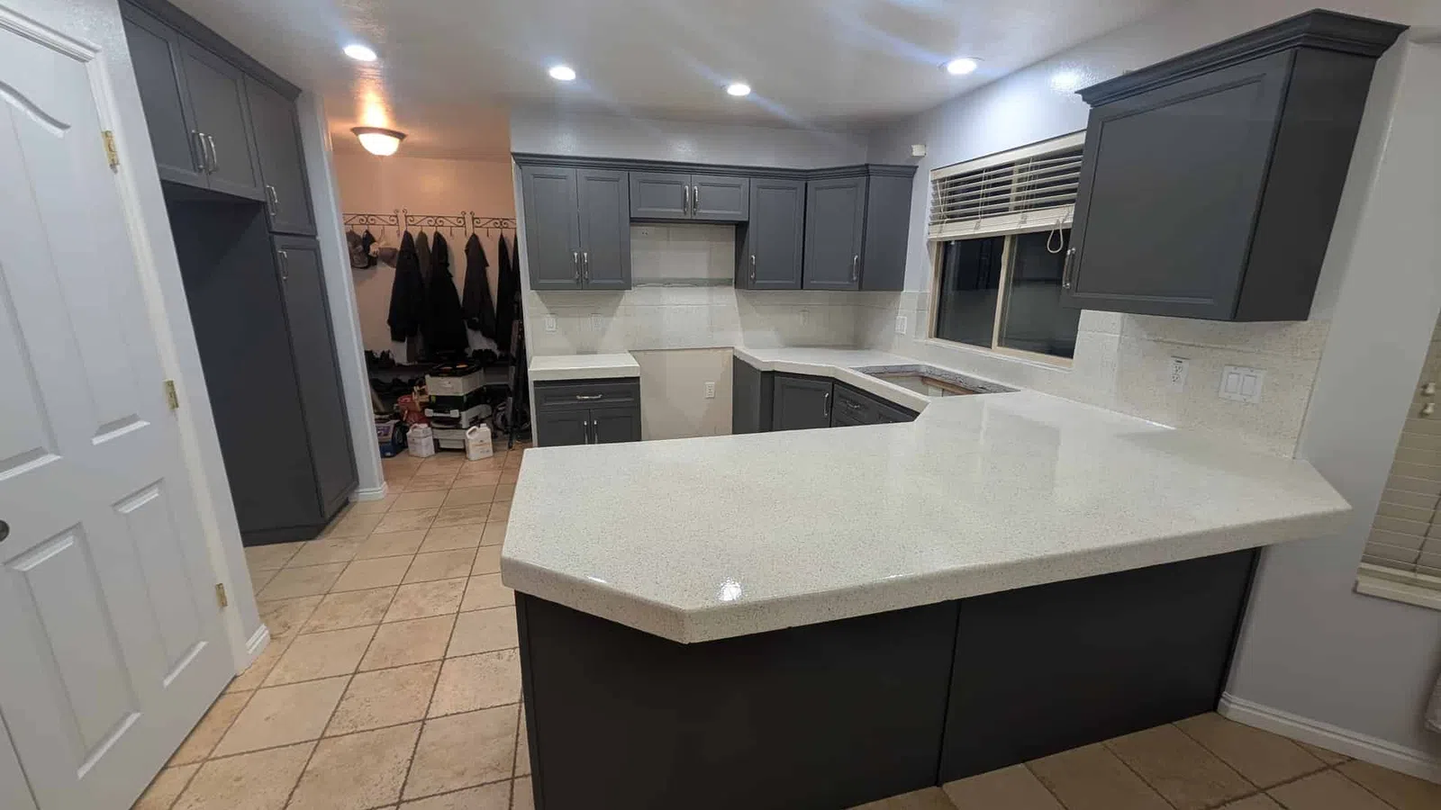 Modern kitchen with dark gray cabinets, large white quartz island, tiled floor, and recessed ceiling lights