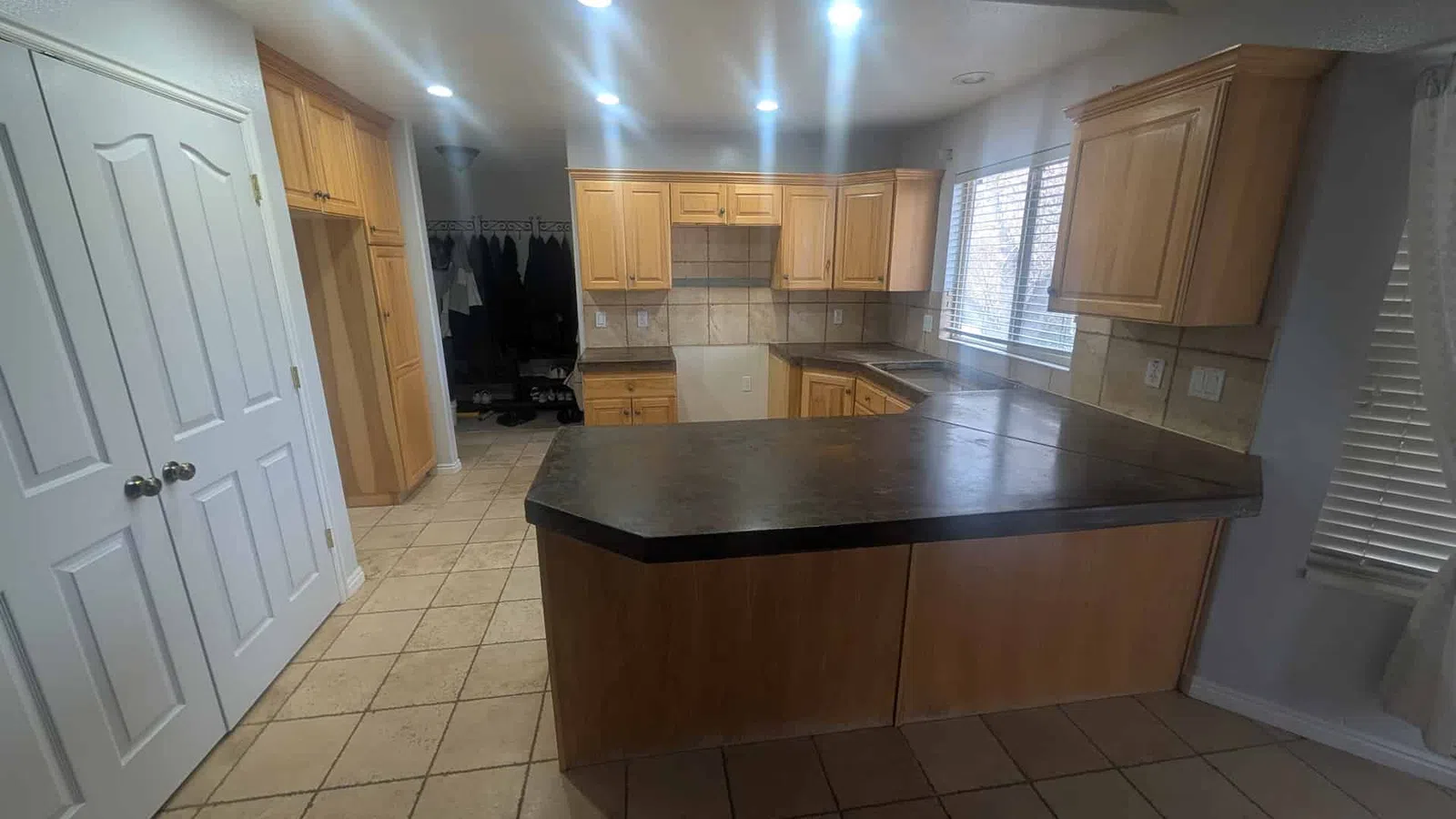 Spacious kitchen with wooden cabinets, tiled floor, large black countertop, and bright ceiling lights.