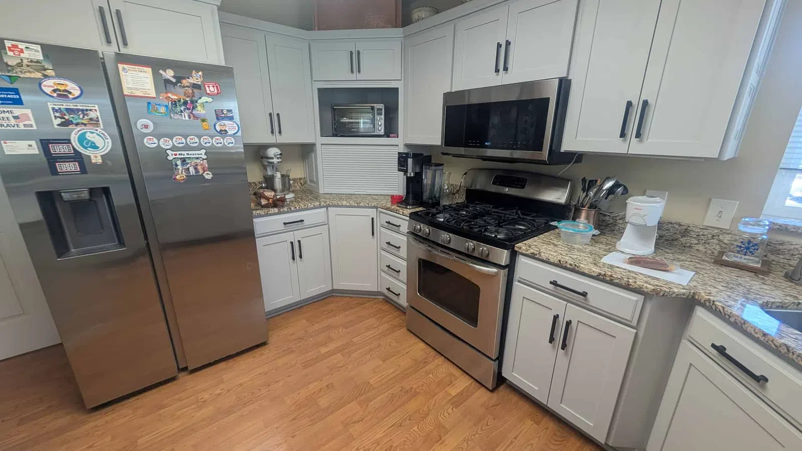 Modern kitchen with stainless steel appliances, light gray cabinets, granite countertops, and wood flooring.
