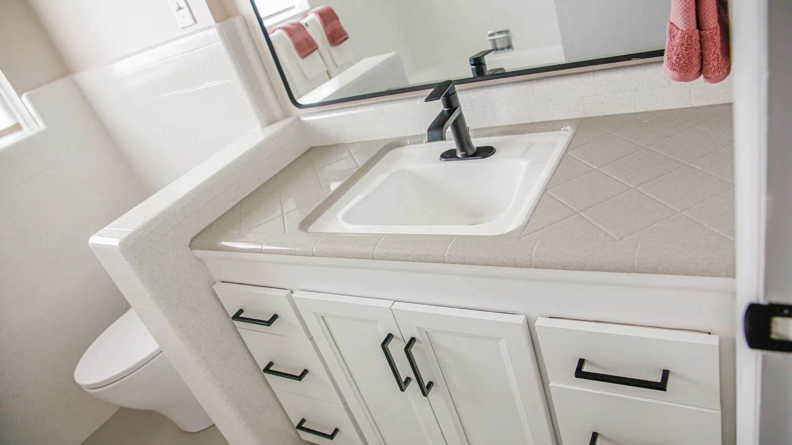 Modern white bathroom vanity with black faucet, tiled countertop, and matching black cabinet handles.