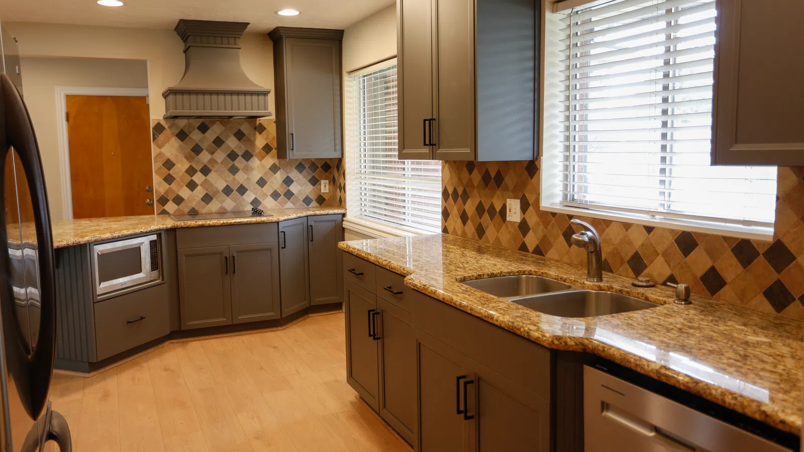 Modern kitchen with granite countertops, gray cabinets, stainless steel appliances, and diamond-patterned tile backsplash.