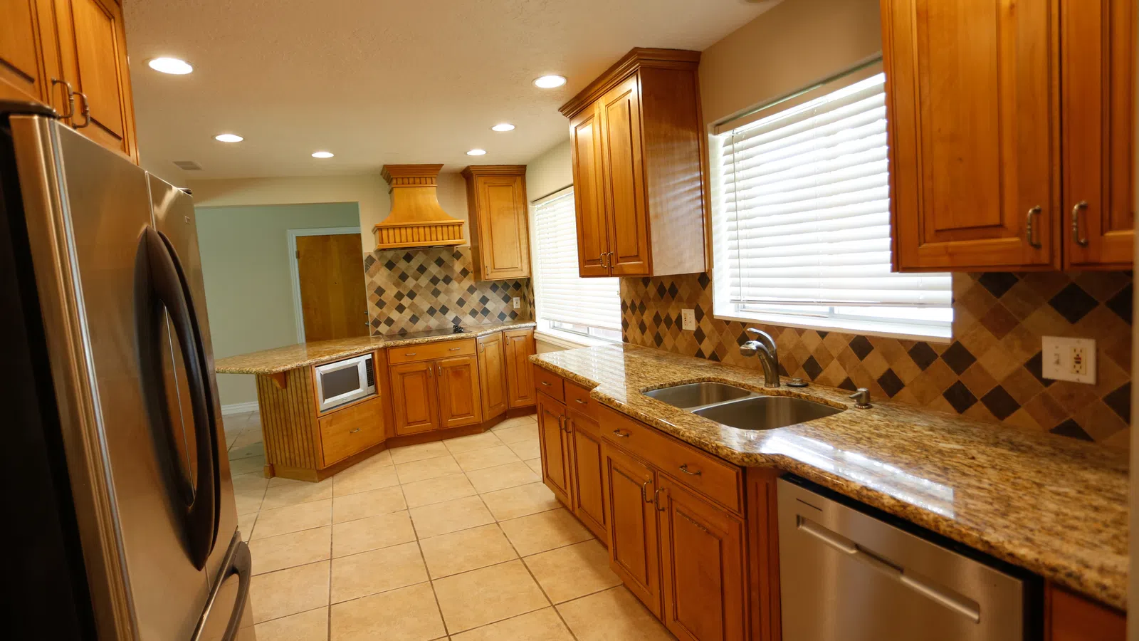 Modern kitchen with wooden cabinets, granite countertops, stainless steel appliances, tiled floor, and mosaic backsplash.
