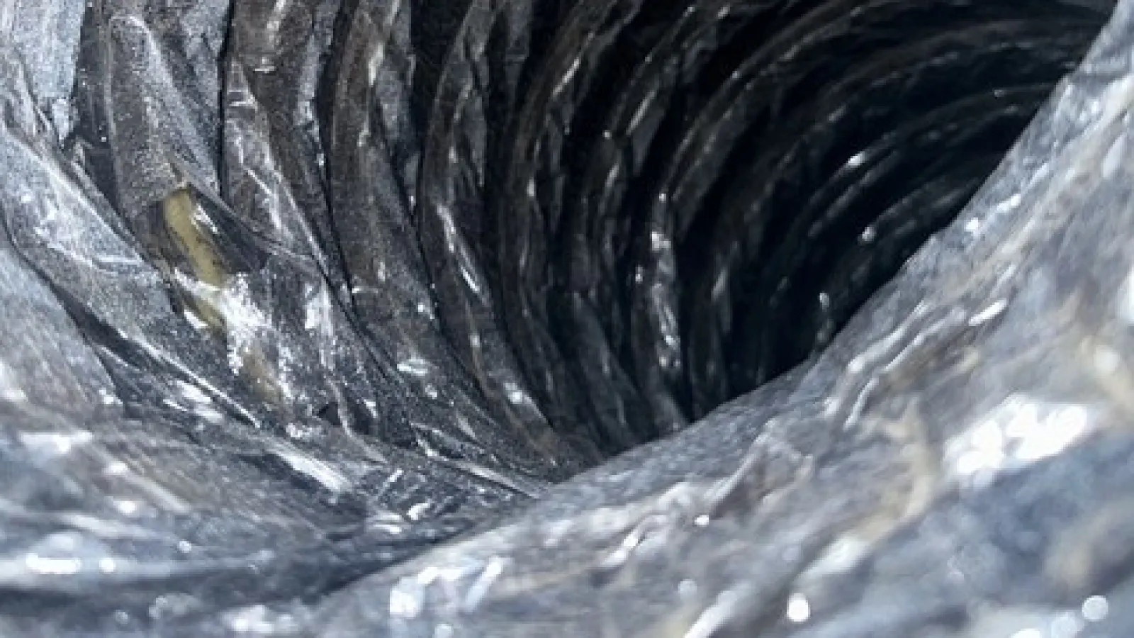 Close-up view inside a flexible metallic duct or ventilation pipe with coiled ridges.