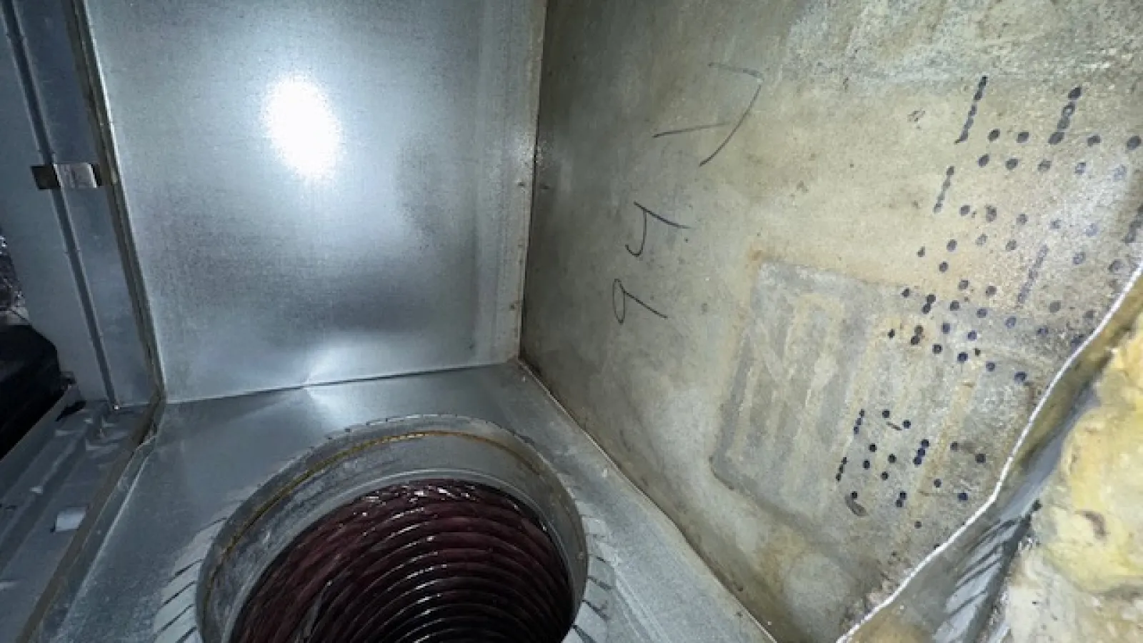 Close-up of a metal duct with a spiral air vent inside a rectangular enclosure showing industrial HVAC components.