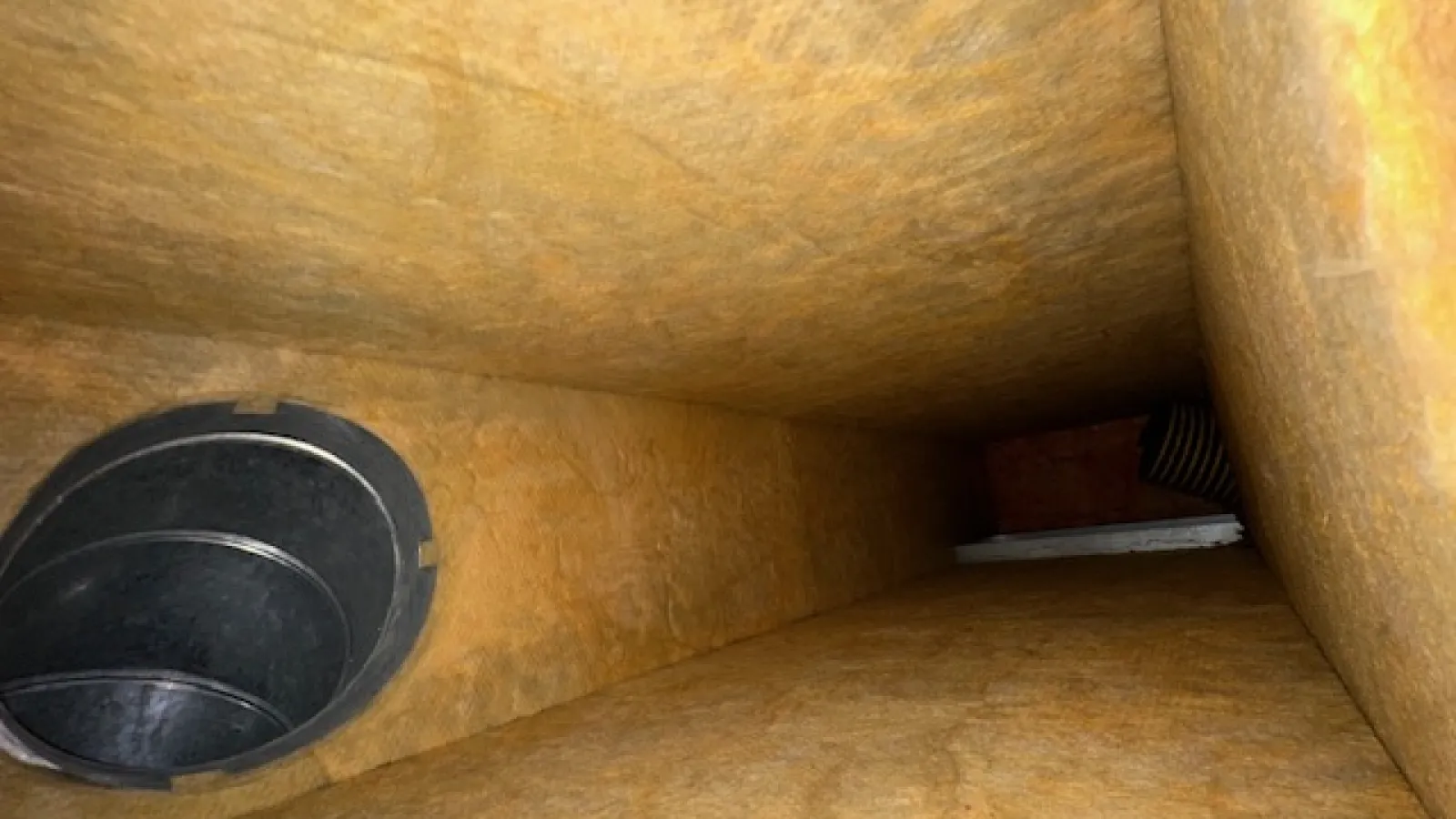 Inside view of an empty rectangular duct with yellow insulation and a circular vent opening on one side.
