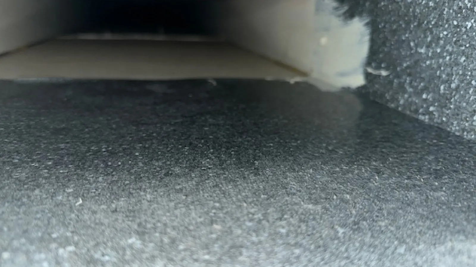 Close-up of a rectangular duct or vent interior with textured gray surface and taped edges.