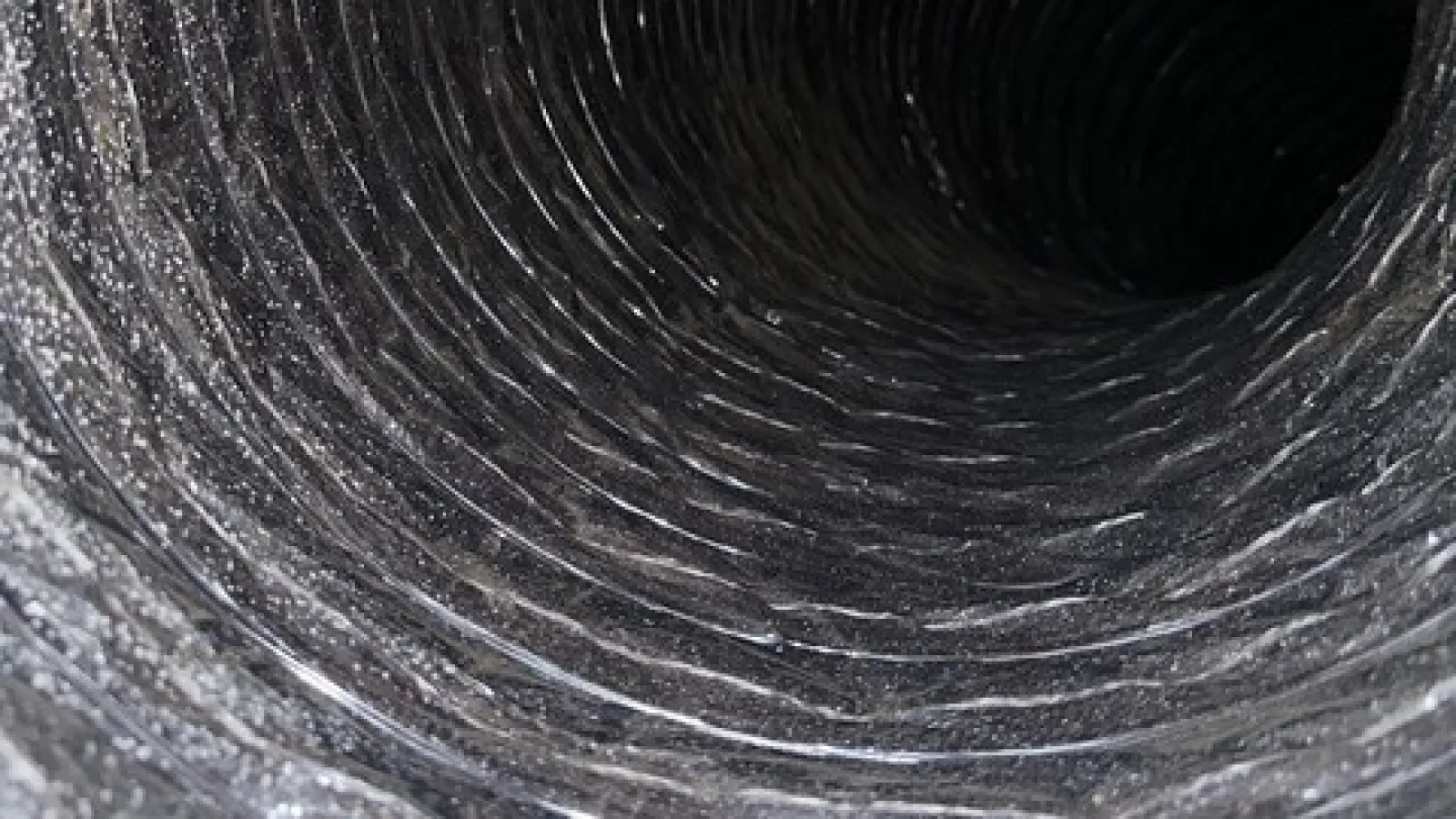 Close-up view inside a dark, coiled flexible duct or hose with textured inner ridges.