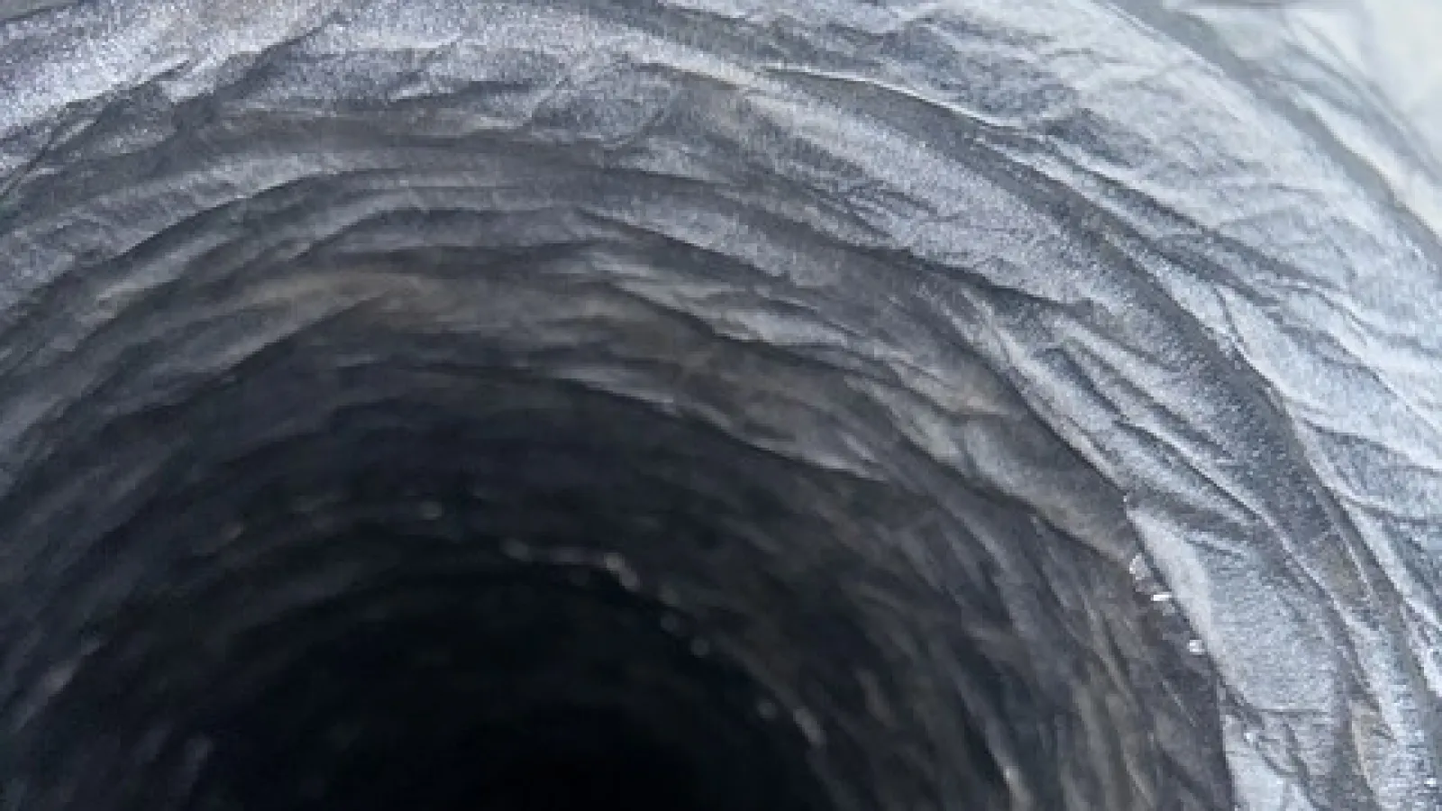 Close-up inside view of a dark, textured tunnel or duct with concentric ridges and rough surface.