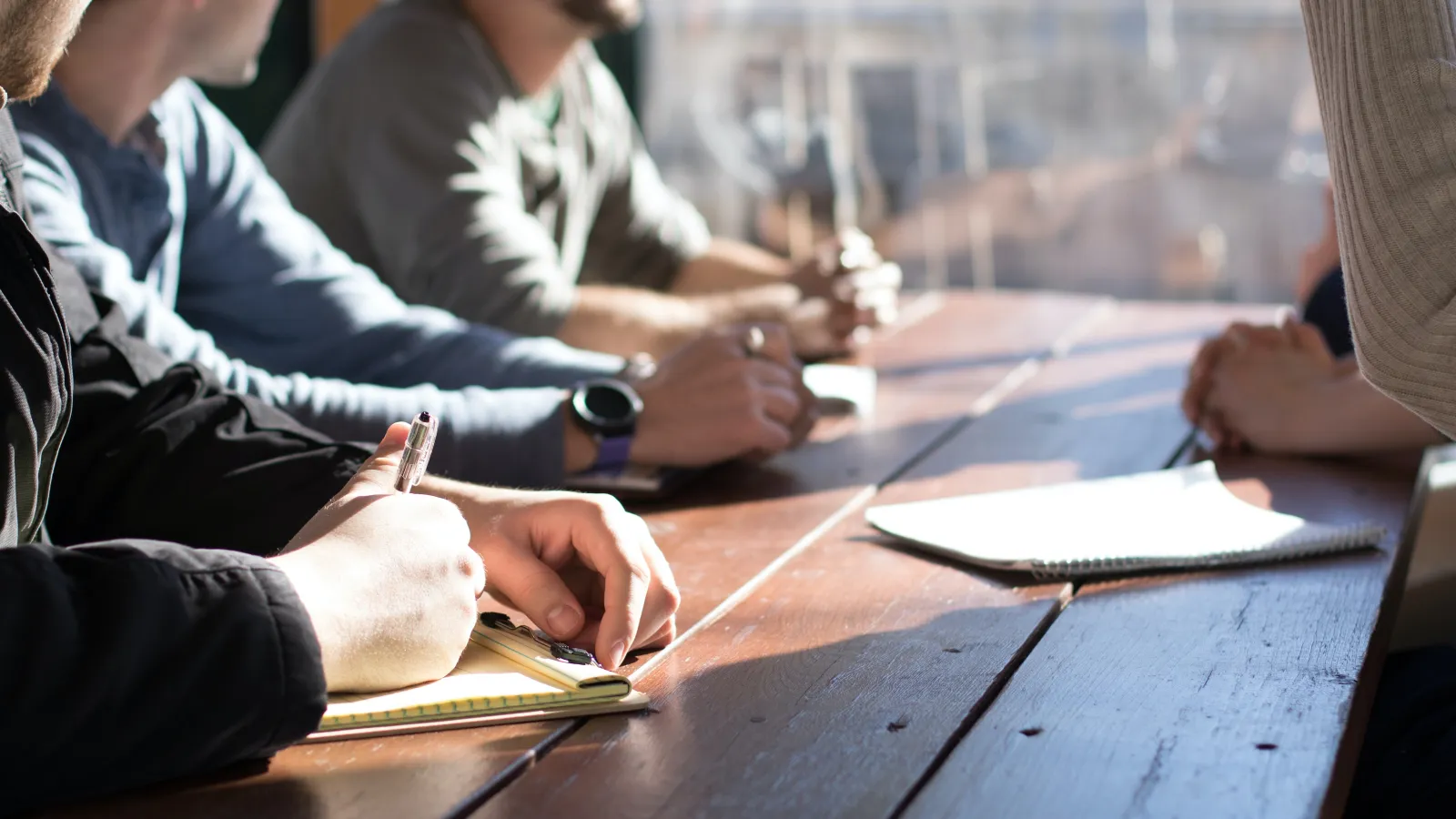 a group of people sitting at a table writing on paper