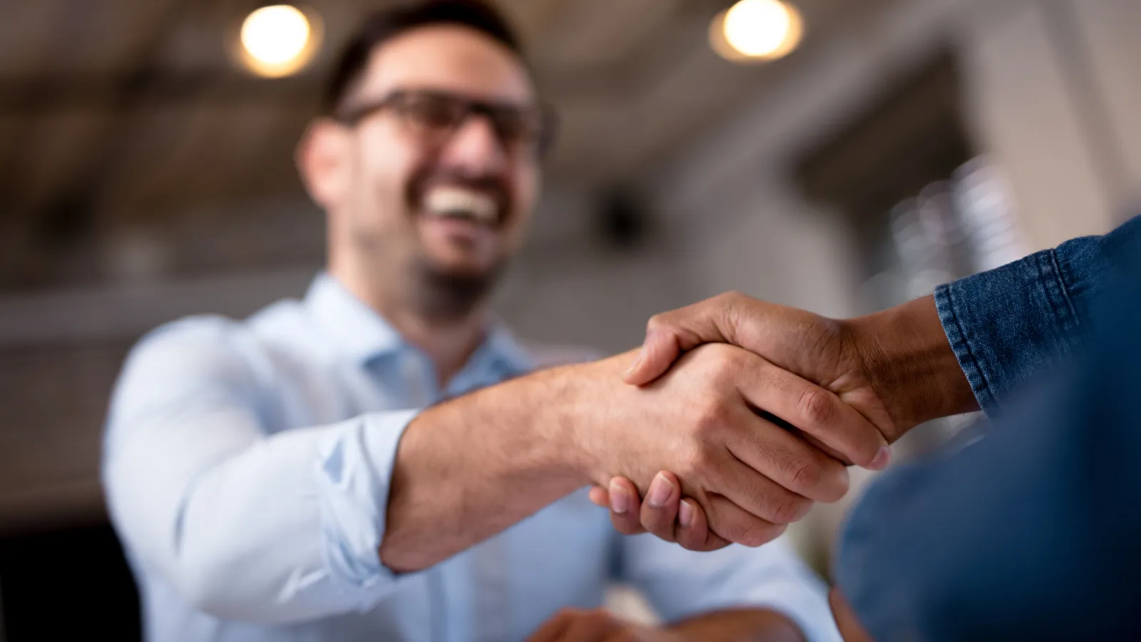 Two people shaking hands in a friendly business meeting with a smiling man wearing glasses.