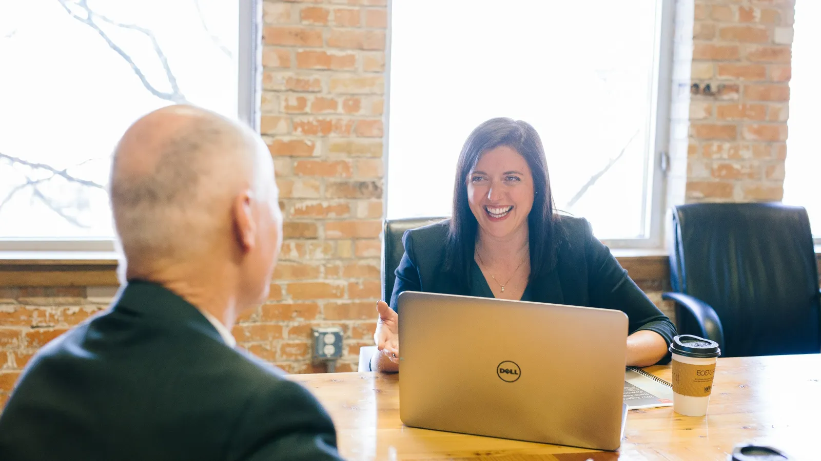 Businesswoman smiling and discussing work with colleague during meeting at wooden conference table