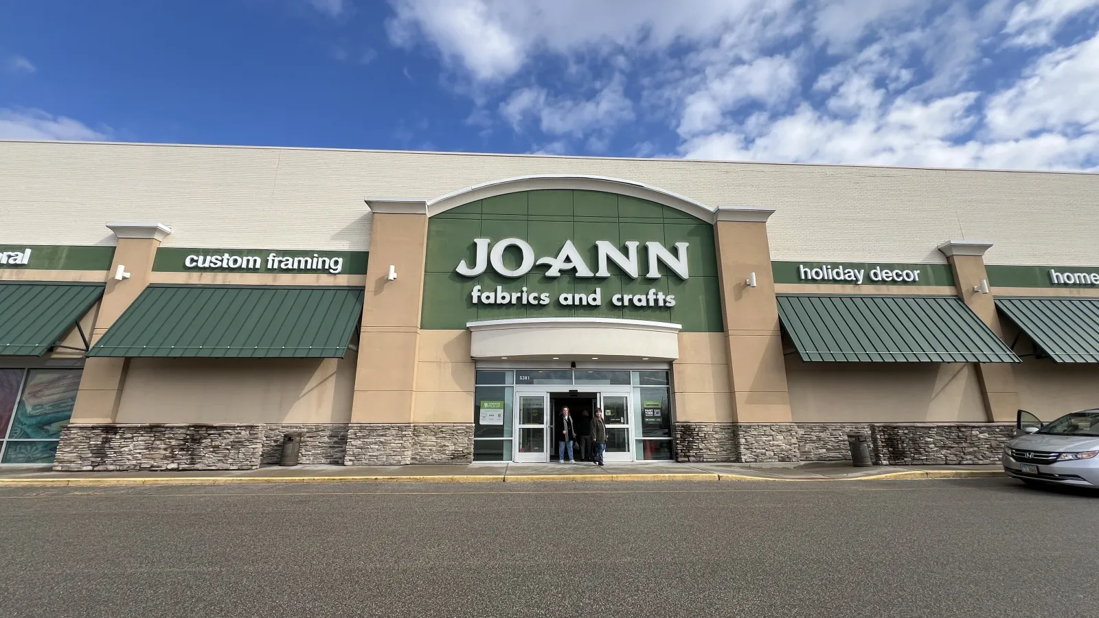 Exterior front view of JOANN fabrics and crafts store with green awnings and clear blue sky.