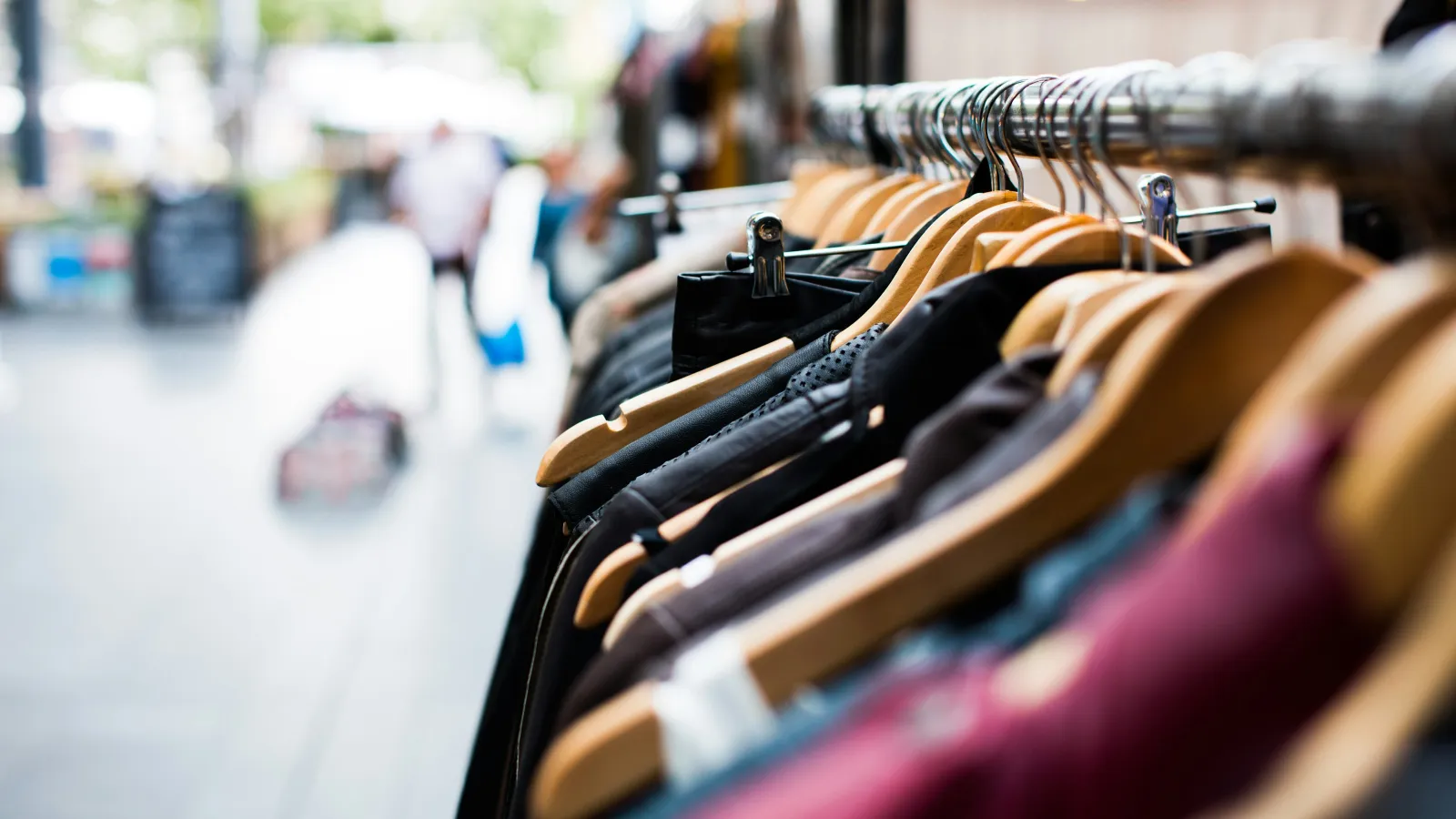 Close-up of clothing on wooden hangers displayed on a metal rack in an outdoor market setting.
