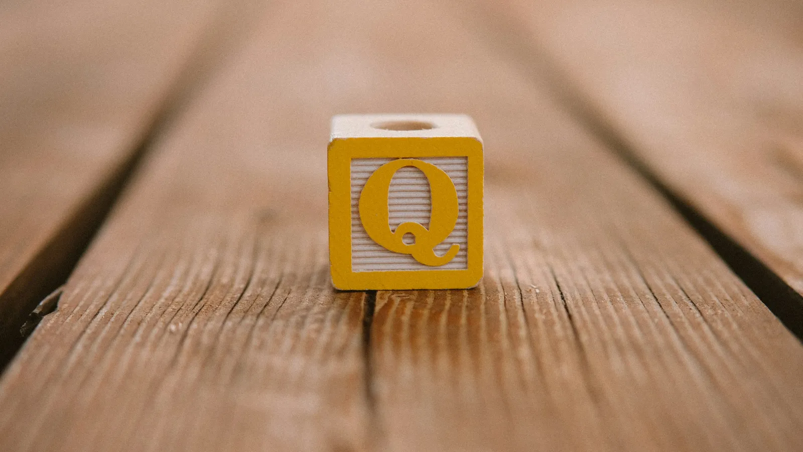 Yellow letter Q block on wooden surface with blurred background