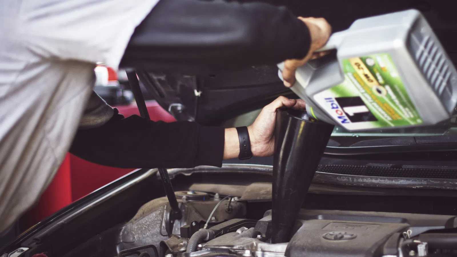 Person pouring motor oil into car engine using a funnel under the open hood of a vehicle.