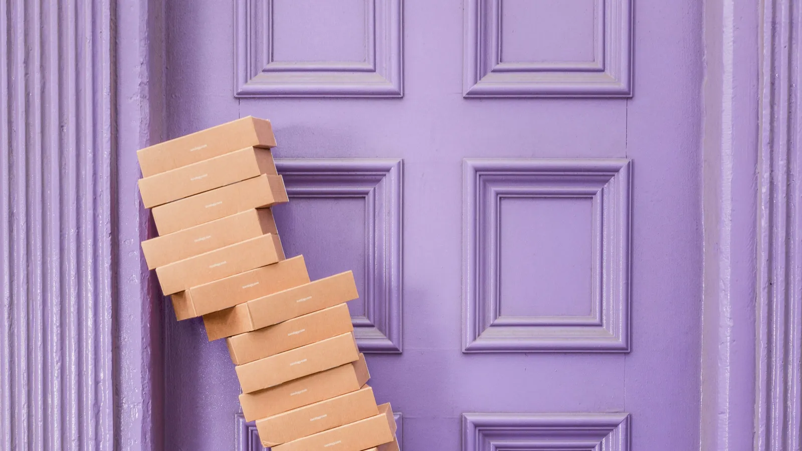 Stack of brown cardboard boxes leaning precariously against a purple ornate wooden door.