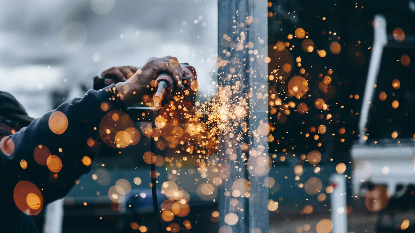 Worker using an angle grinder producing sparks while cutting metal outdoors with bokeh effects