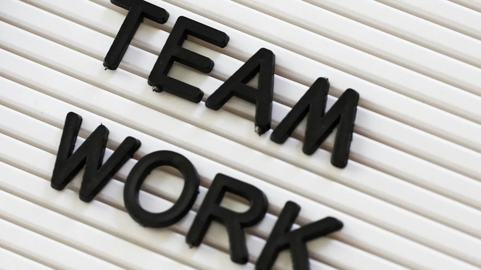 Black letters spelling TEAM WORK on a white ridged board symbolizing collaboration.