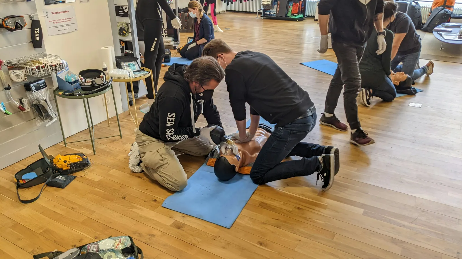 People practicing CPR on mannequins during a first aid training session in a spacious room with equipment.