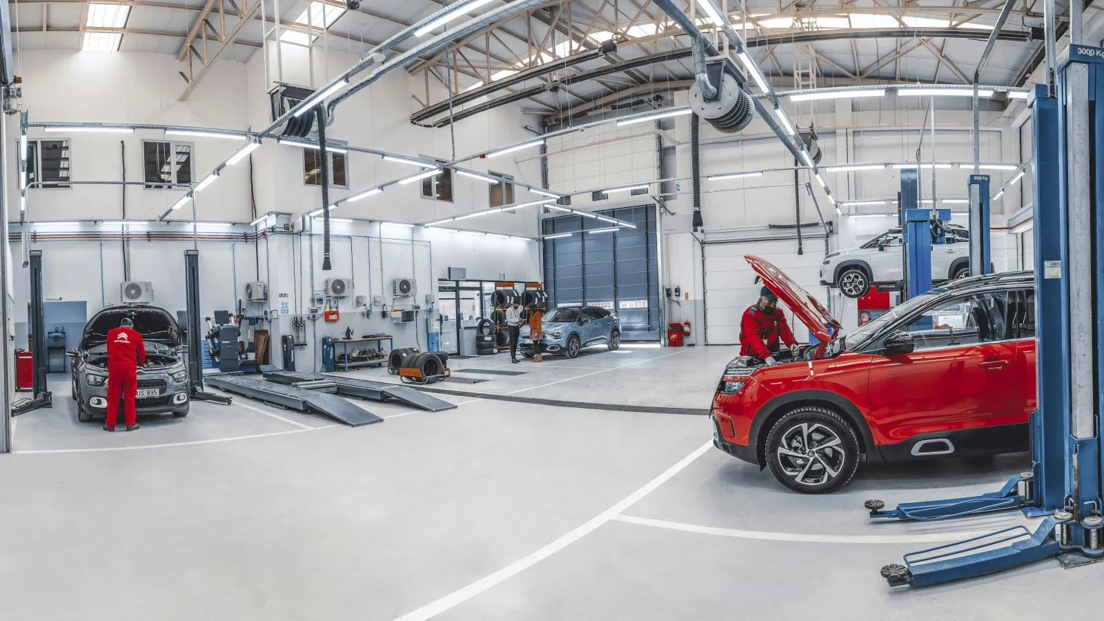 Bright automotive workshop with mechanics inspecting cars and using vehicle lifts in a spacious garage.