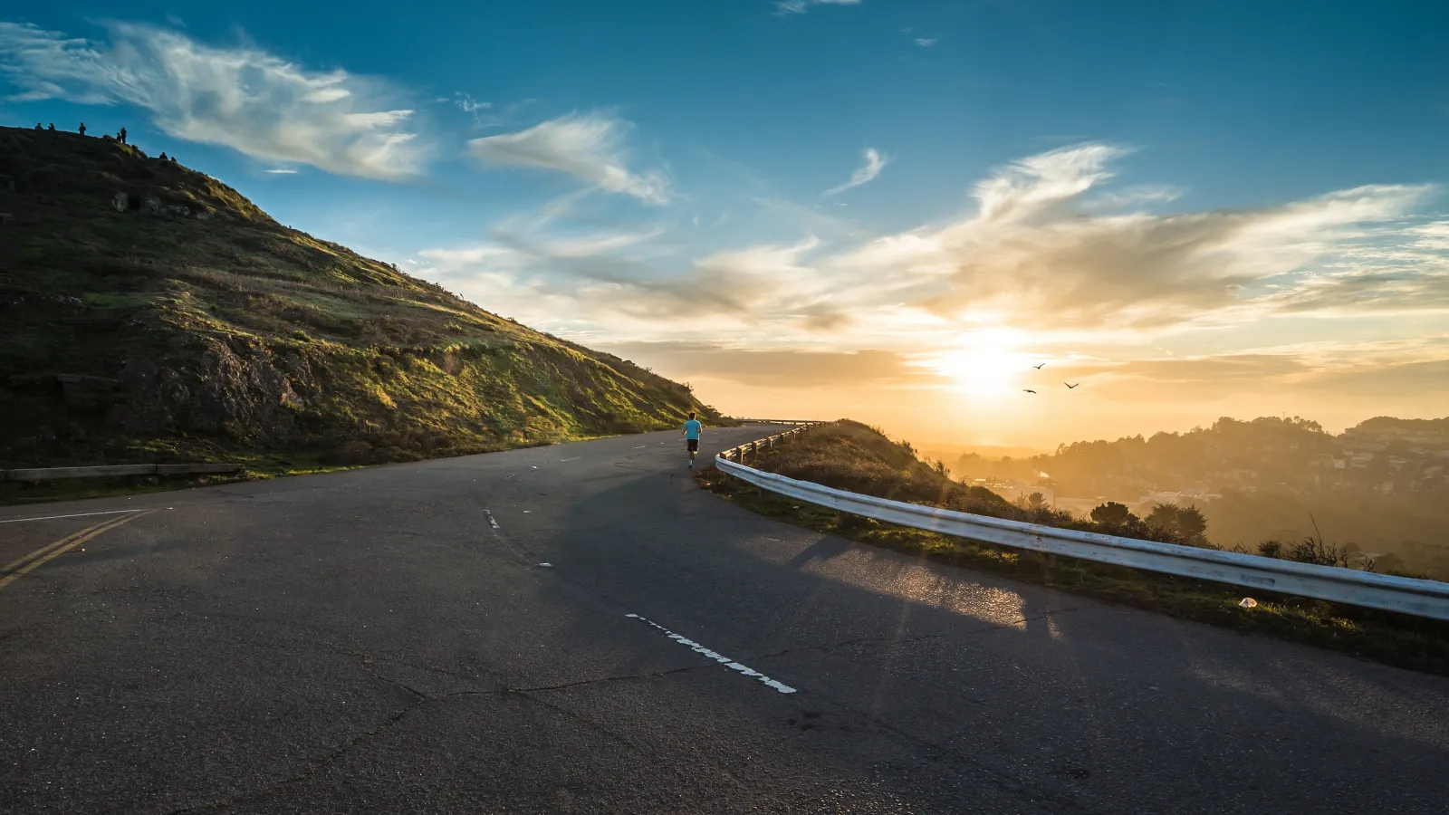 Runner jogging on winding road at sunset with hills and birds in the sky