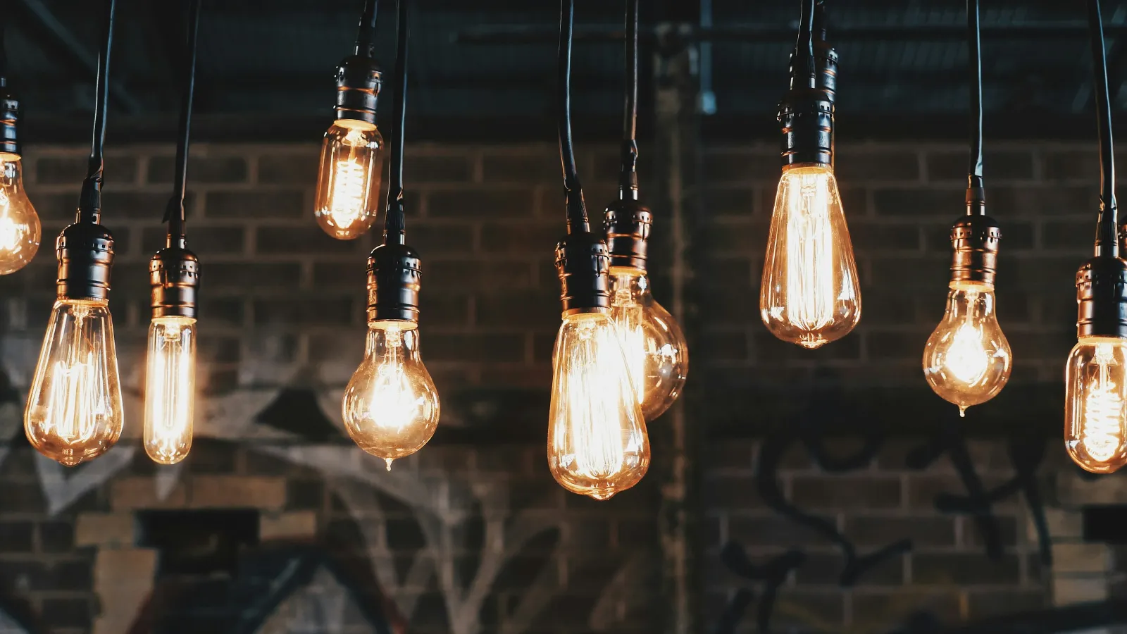 Hanging vintage Edison light bulbs glowing warmly against a dark brick wall with graffiti background