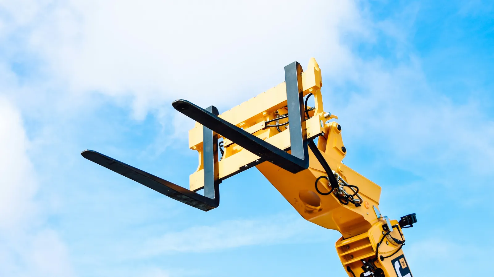 Yellow forklift lifting mechanism with black forks extended against a blue sky background