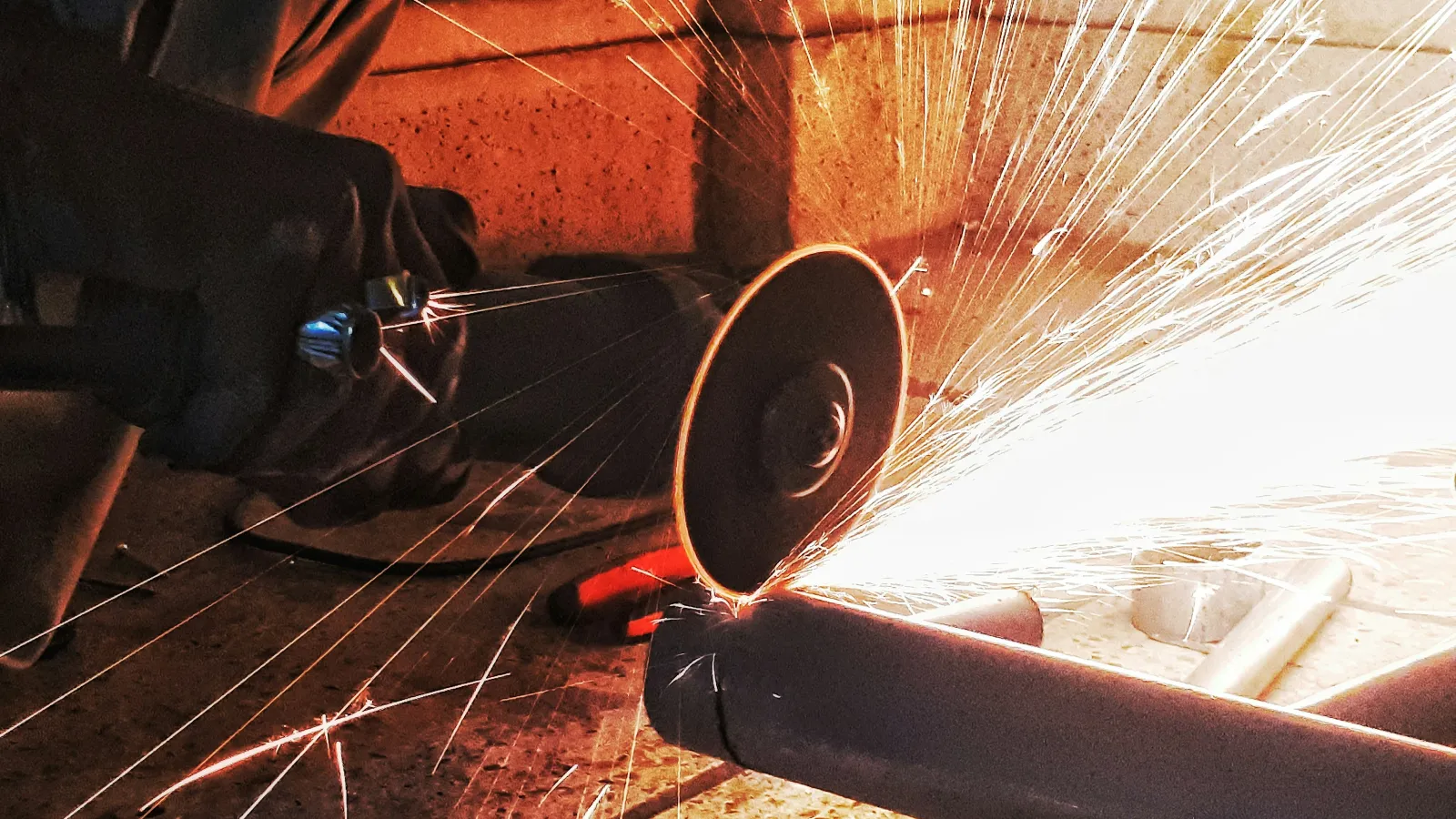 Close-up of a worker cutting metal pipe with a grinder, creating bright sparks in a workshop.