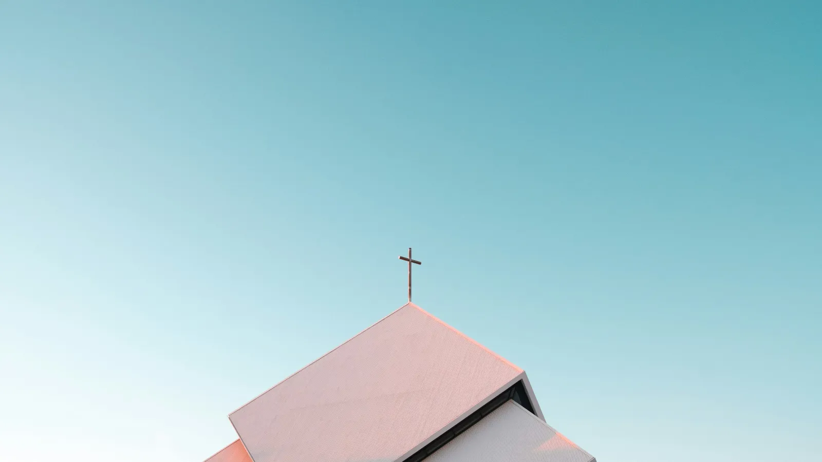 Modern church building with angular roof and cross against clear blue sky at sunset.