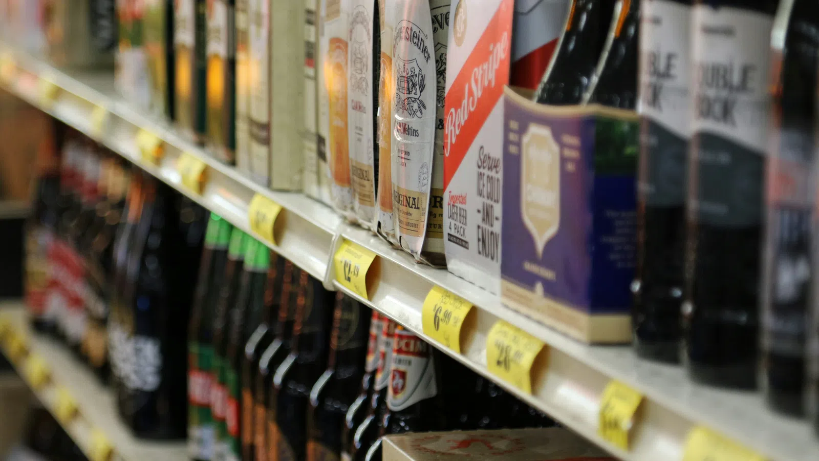 Shelves stocked with a variety of bottled and canned beers in a grocery store with price tags visible.