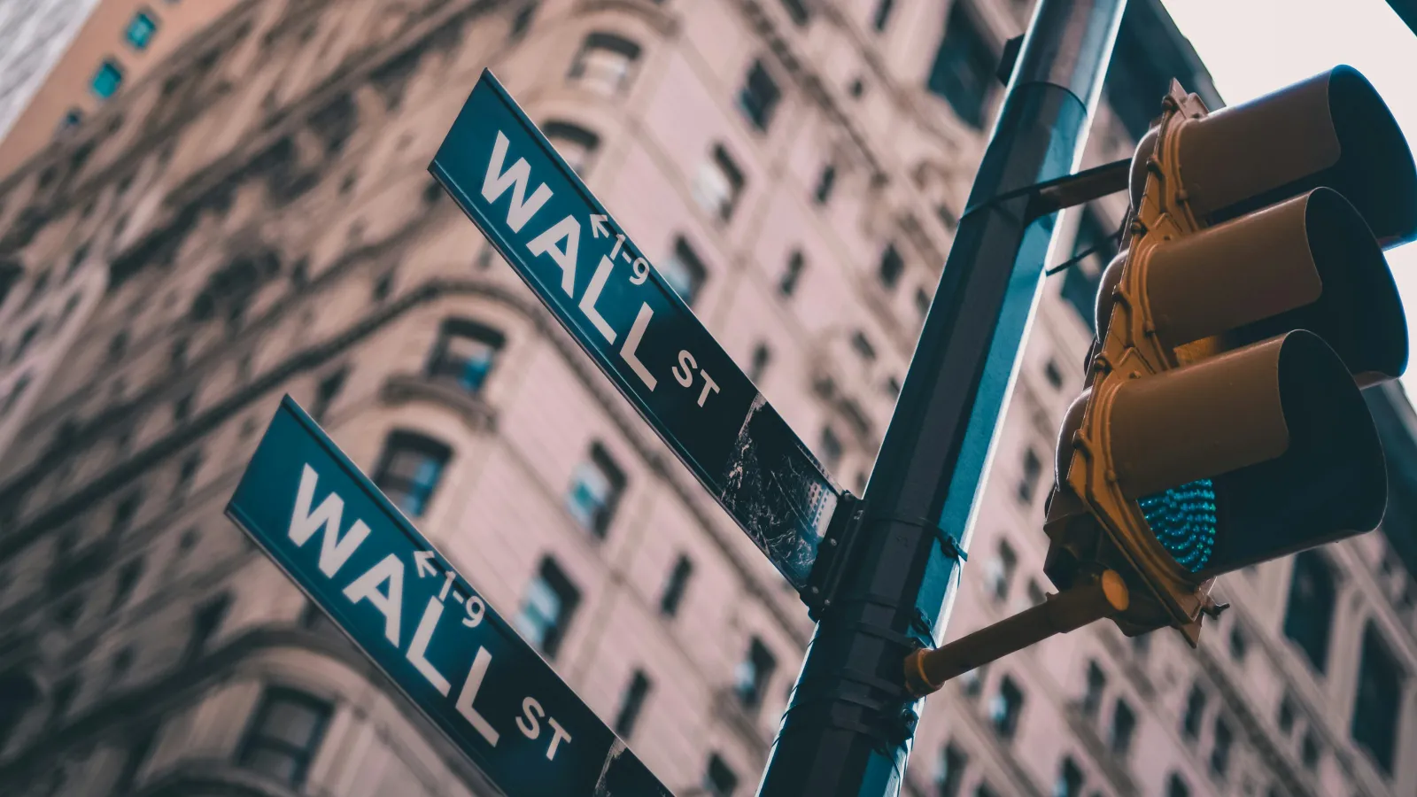 Street signs for Wall Street on a pole with a city building and traffic light in the background