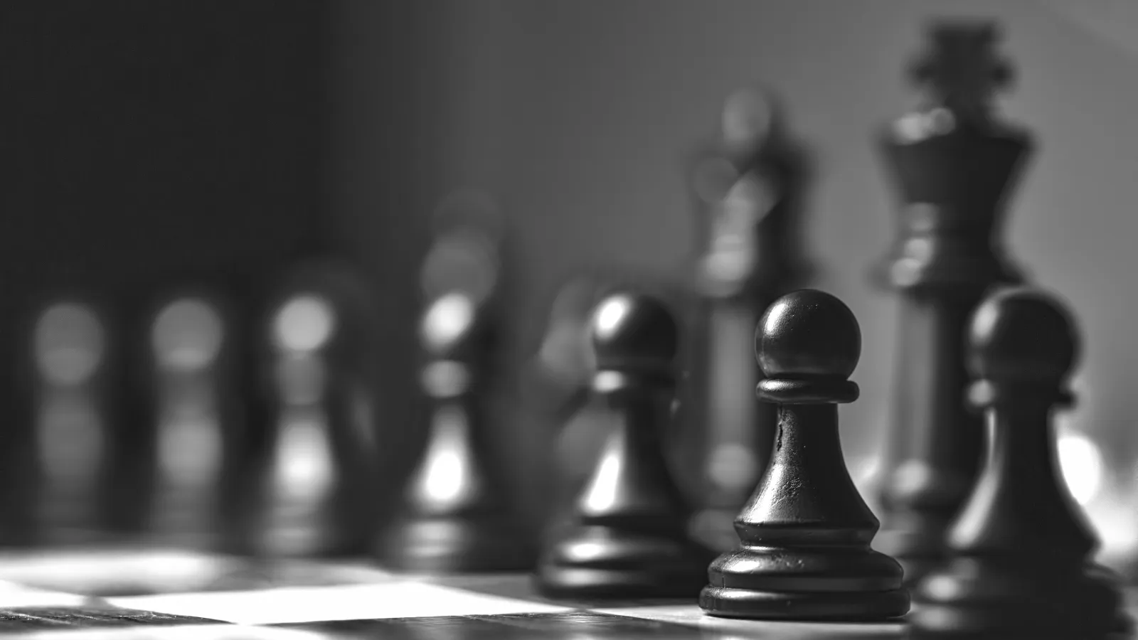 Black chess pawns in focus on a chessboard with blurred king and other pieces in the background.