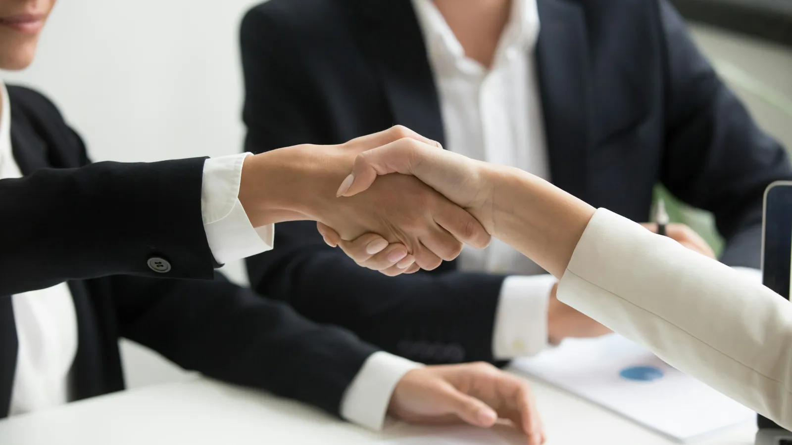 Close-up of two business professionals shaking hands over table with documents, symbolizing agreement and partnership.