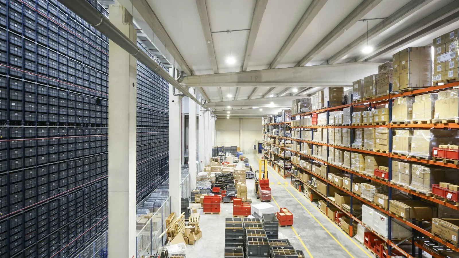 Large warehouse interior with tall shelves stacked with boxes and organized storage bins under bright lighting.