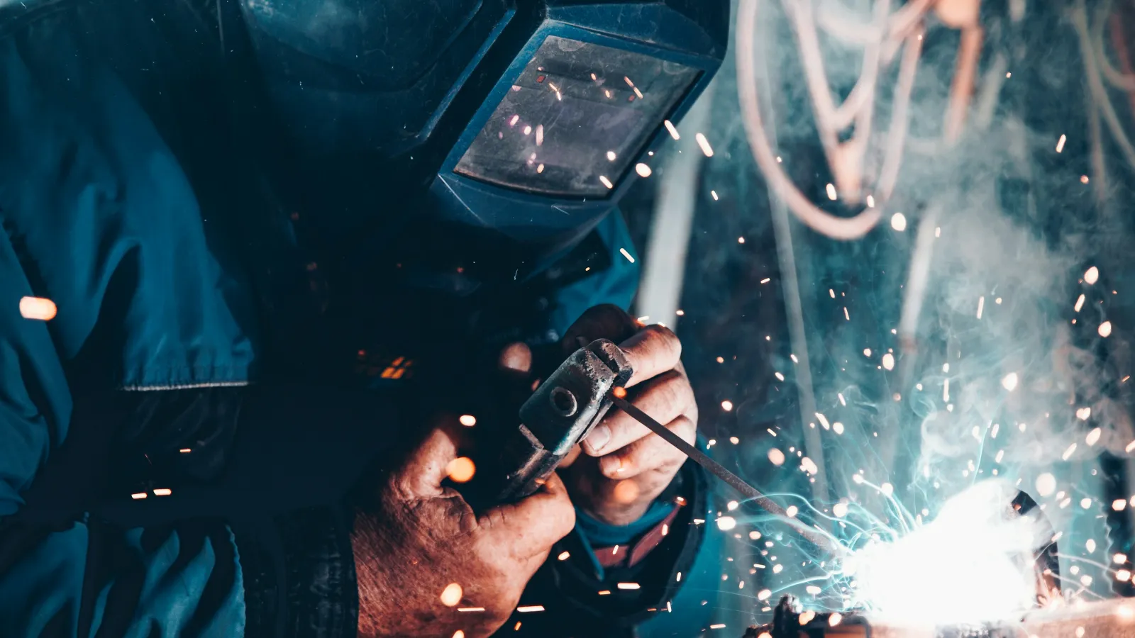 Welder wearing protective gear sparks flying while welding metal in a workshop environment