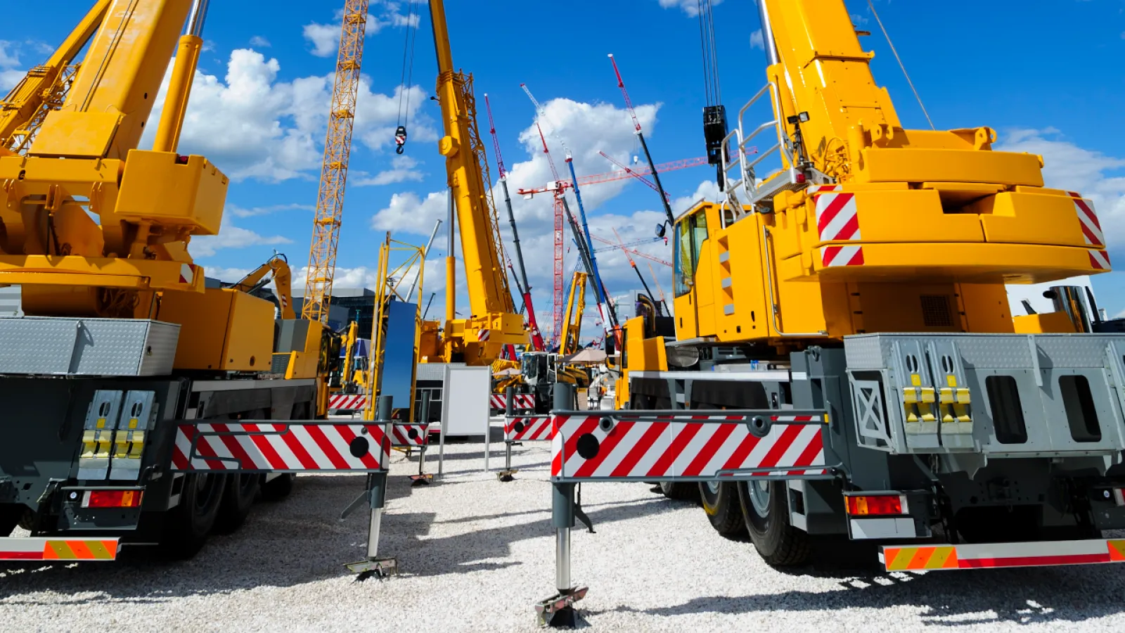 A construction site filled with yellow cranes under a bright blue sky, showcasing heavy machinery and equipment.