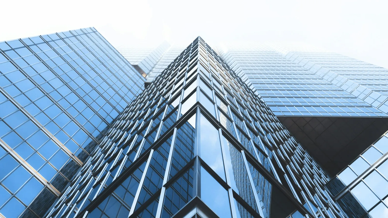Upward view of modern glass skyscrapers with reflective windows against a bright sky.