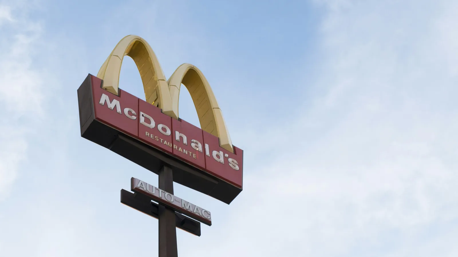 Tall McDonald's restaurant sign with golden arches against a blue sky background